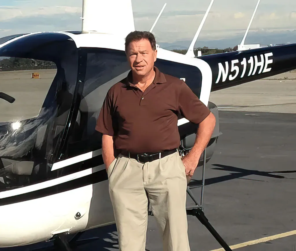 Michael Bisek, founder of Helicopter Experts, standing in front of his Robinson R-44 Raven I or Robinson R-44 Raven II helicopter N511HE